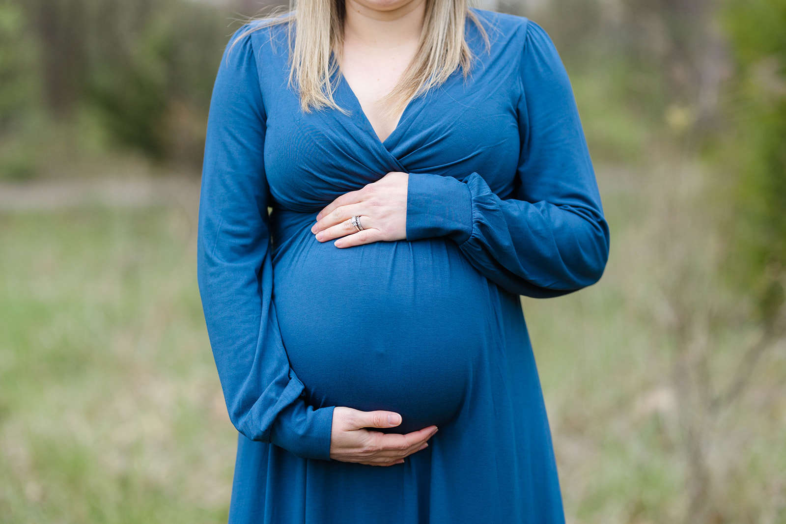 Details of a mom to be holding her bump in a blue maternity dress