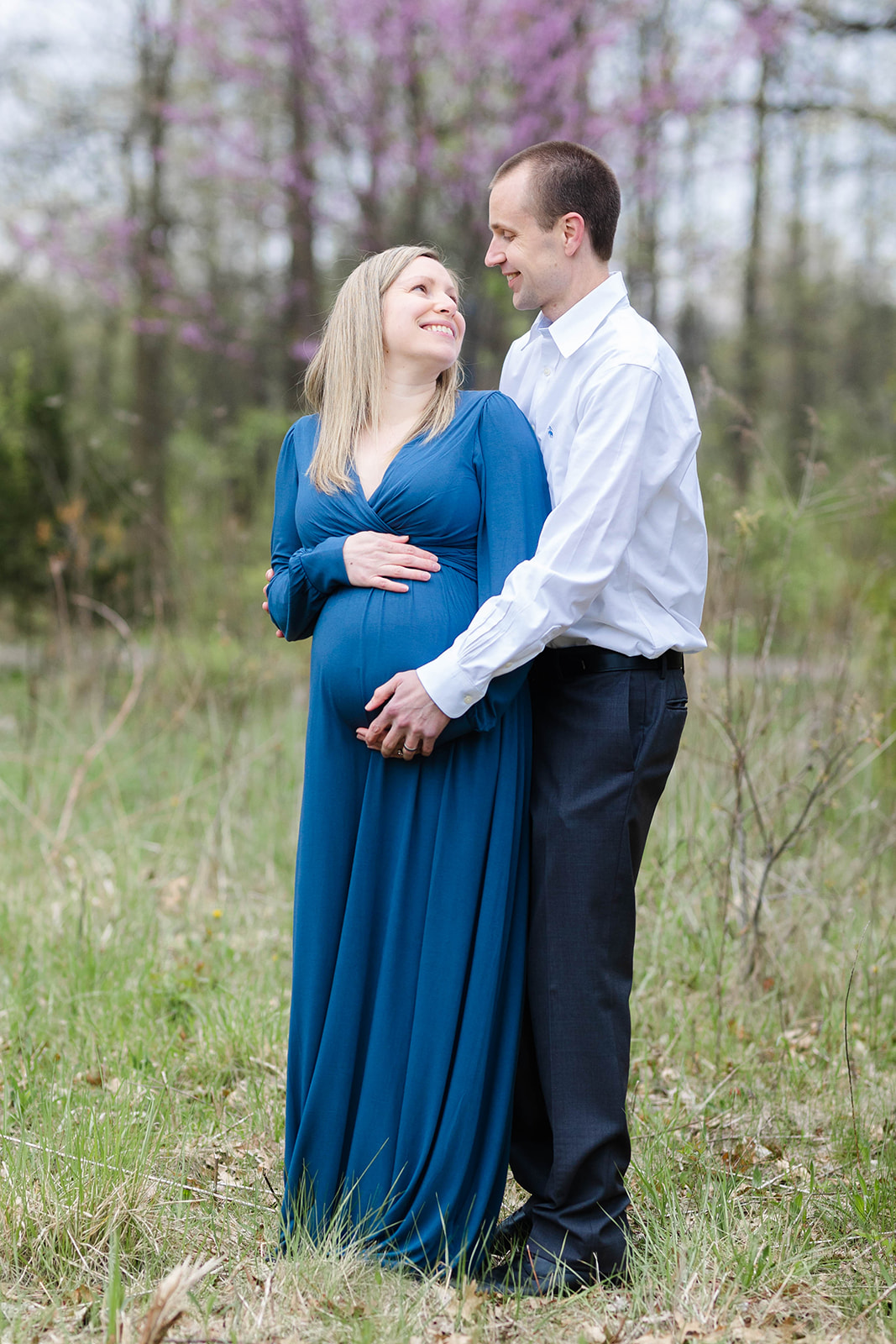 A mother to be stands in a forest looking up at her husband hugging her from behind Doulas Columbus Ohio