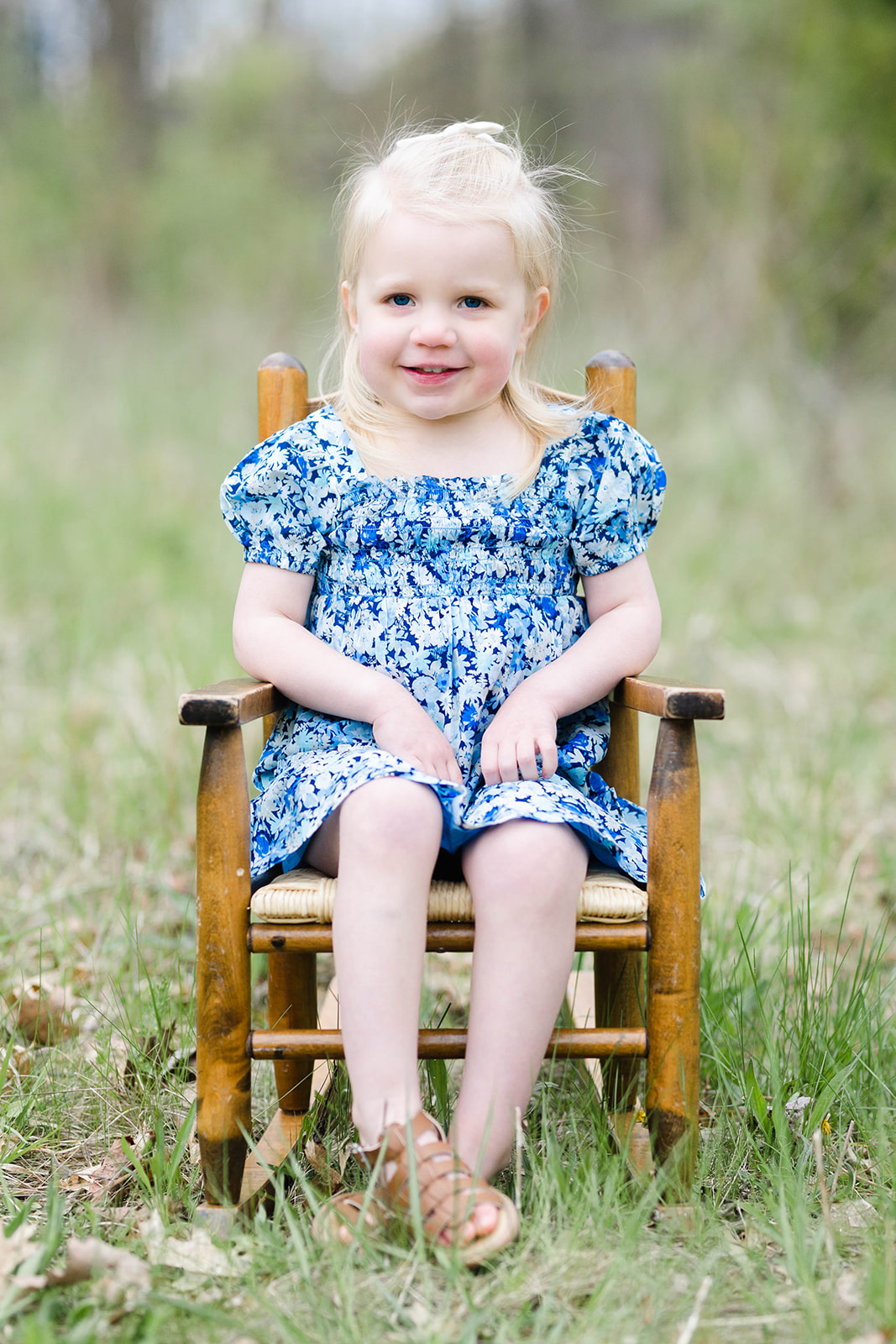 A young girl sits in an antique wooden rocking chair in a grassy field in a blue dress Baby Stores in Columbus Oh