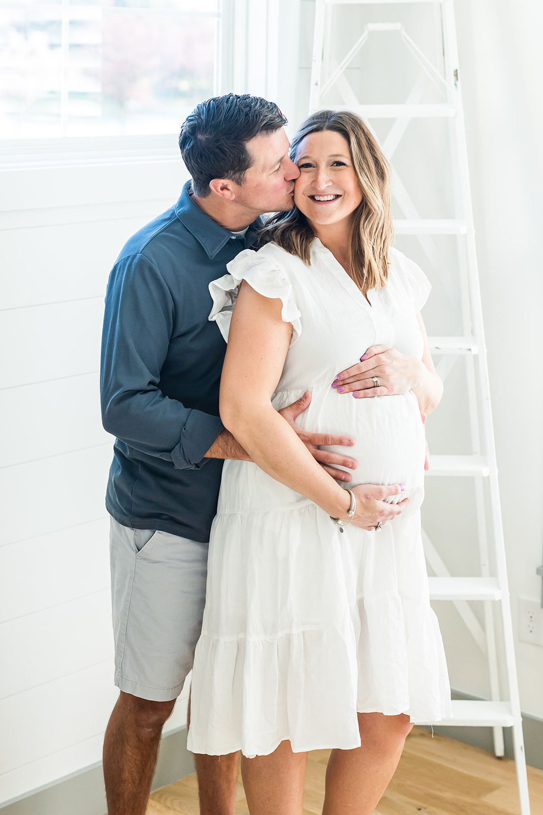 A father leans in kissing the cheek of his pregnant wife while hugging her bump lactation consultant columbus ohio