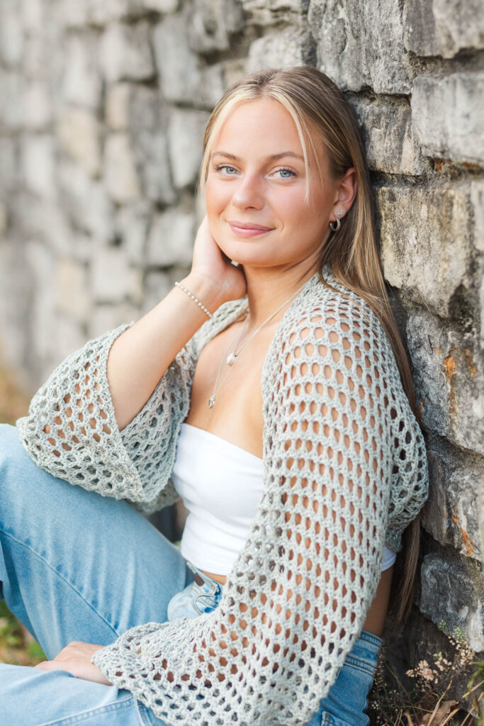 Senior girl softly smiling while leaning against a wall, demonstrating natural posing during senior session