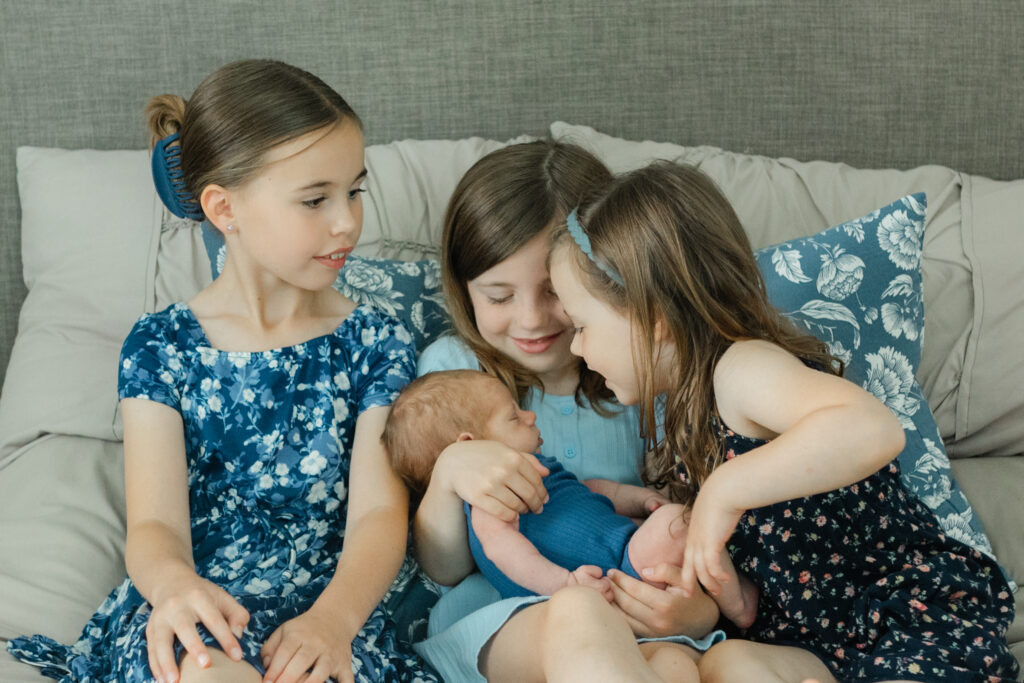 3 sisters holding and looking admiringly at their baby brother
